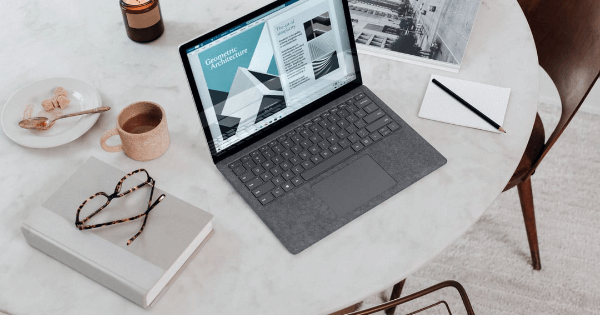 A table with a laptop, book and a cup of coffee on it