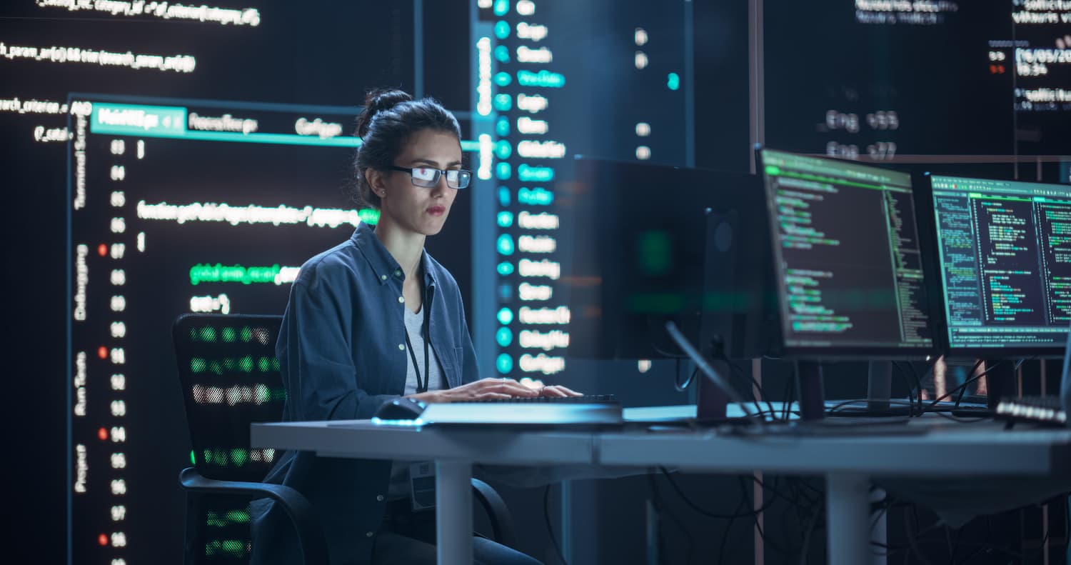 Mujer sentada en un escritorio con múltiples pantallas de computadora, trabajando en el Monitoreo LAN&WAN.