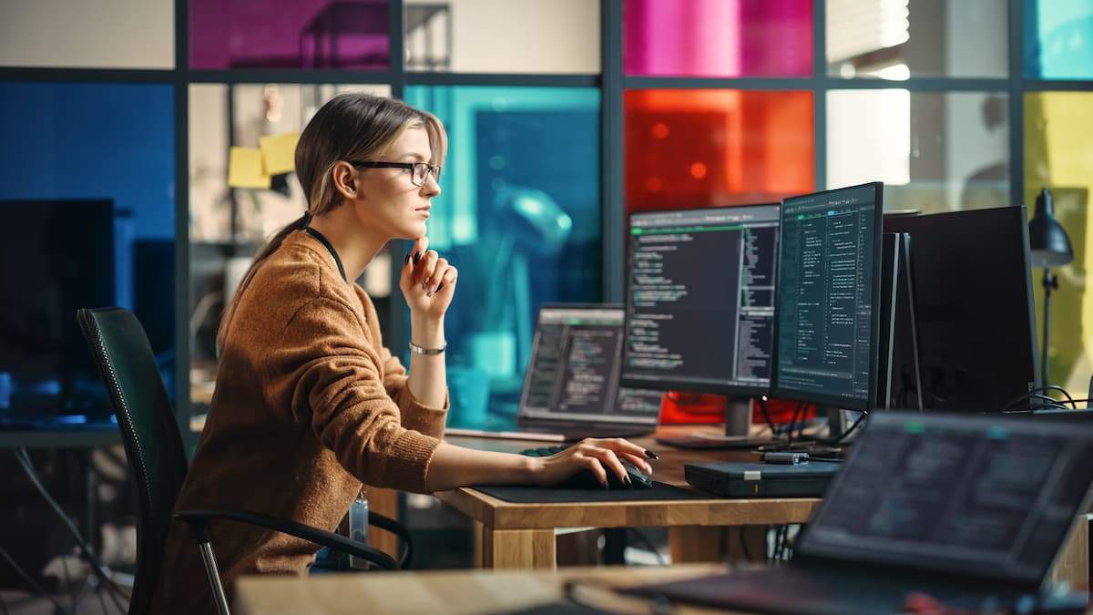 Una mujer sentada en un escritorio con una computadora y un monitor, navegando por internet.