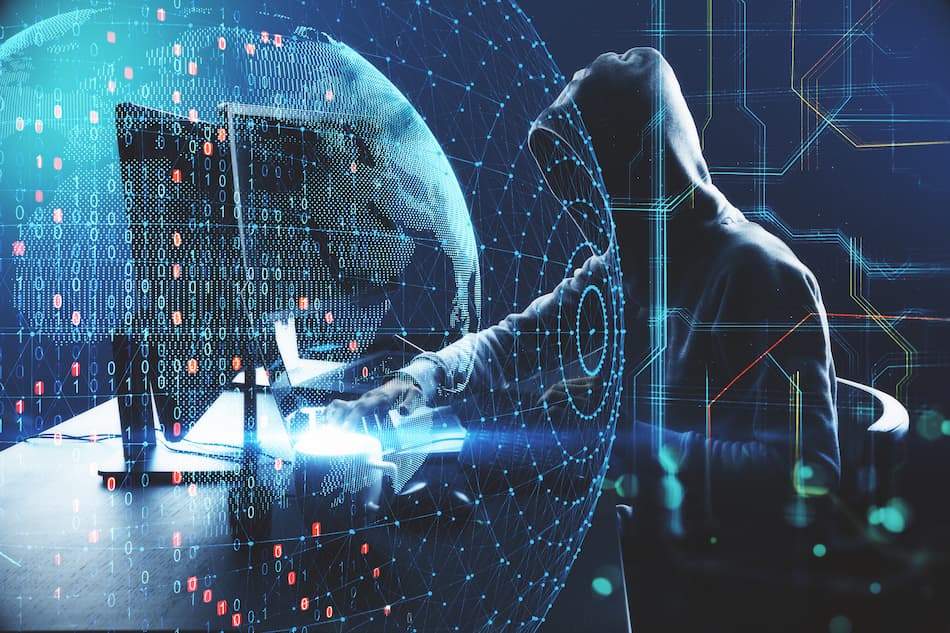 A person in a hoodie sits at a computer, focused on their work, possibly related to cybersecurity or phishing awareness.