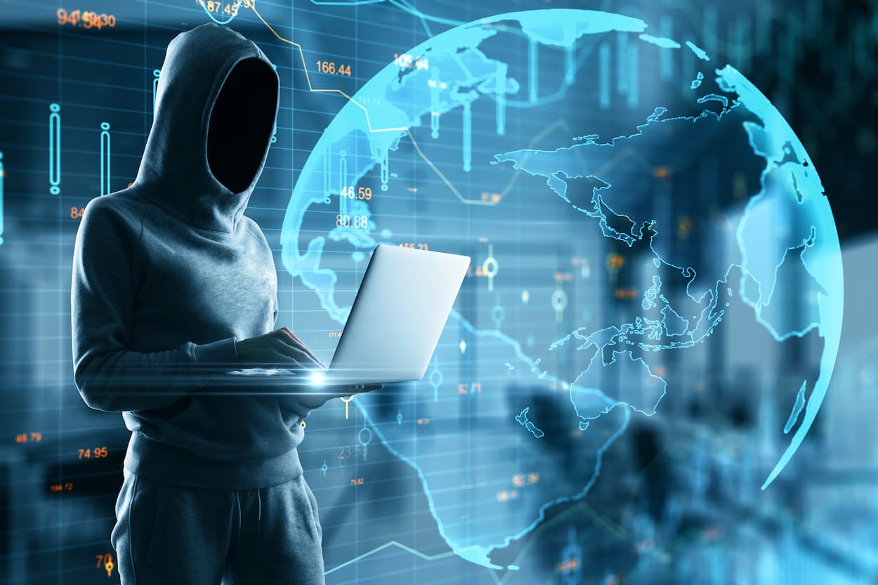 acker con sudadera trabajando en laptop, fondo de mapa mundial, representando el concepto de ciberseguridad y anti-DDoS.