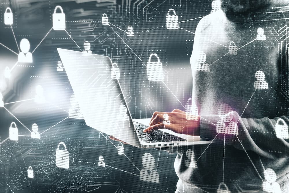 Hombre usando un portátil con íconos de ciberseguridad en el fondo, representando la protección contra ataques DDoS.