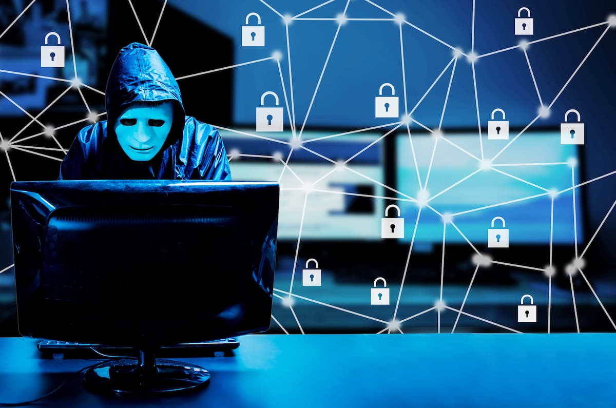Persona con capucha y máscara frente a una computadora, representando un acto de phishing o cibercriminalidad.