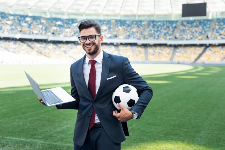 Empresario en traje sostiene una laptop y un balón de fútbol, simbolizando la conexión entre tecnología Anti-DDos y deporte.